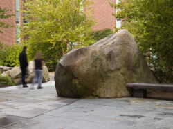 <a href="https://landscapearchitecturebuilt.com/staging/keene-state-college">Keene State College: Natural Science Center Courtyard</a>, <br>Keene, NH, USA An image of a landscape architecture project at Keene State College, showing a large boulder beside a wood bench, cutting into stone paving