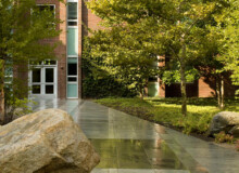 <a href="https://landscapearchitecturebuilt.com/staging/keene-state-college">Keene State College: Natural Science Center Courtyard</a>, <br>Keene, NH, USA An image of a landscape architecture project at Keene State College, showing a paved pathway with a feature boulder to the left of walkway