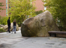 <a href="https://landscapearchitecturebuilt.com/keene-state-college">Keene State College: Natural Science Center Courtyard</a>, <br>Keene, NH, USA An image of a landscape architecture project at Keene State College, showing a large boulder beside a wood bench, cutting into stone paving