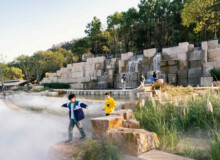<a href="https://landscapearchitecturebuilt.com/tangshan-ape-man-cave">Tangshan Ape Man Cave</a>, <br>Nanjing, China Landscape architecture project in China showing a large water feature with rough cut boulders and grasses along edge. A large sculptural stone water fall is beyond.